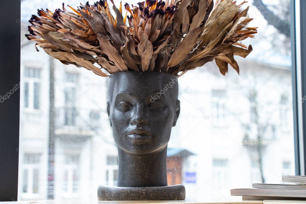 vase in the shape of a person's face with a bouquet of dried exotic flowers