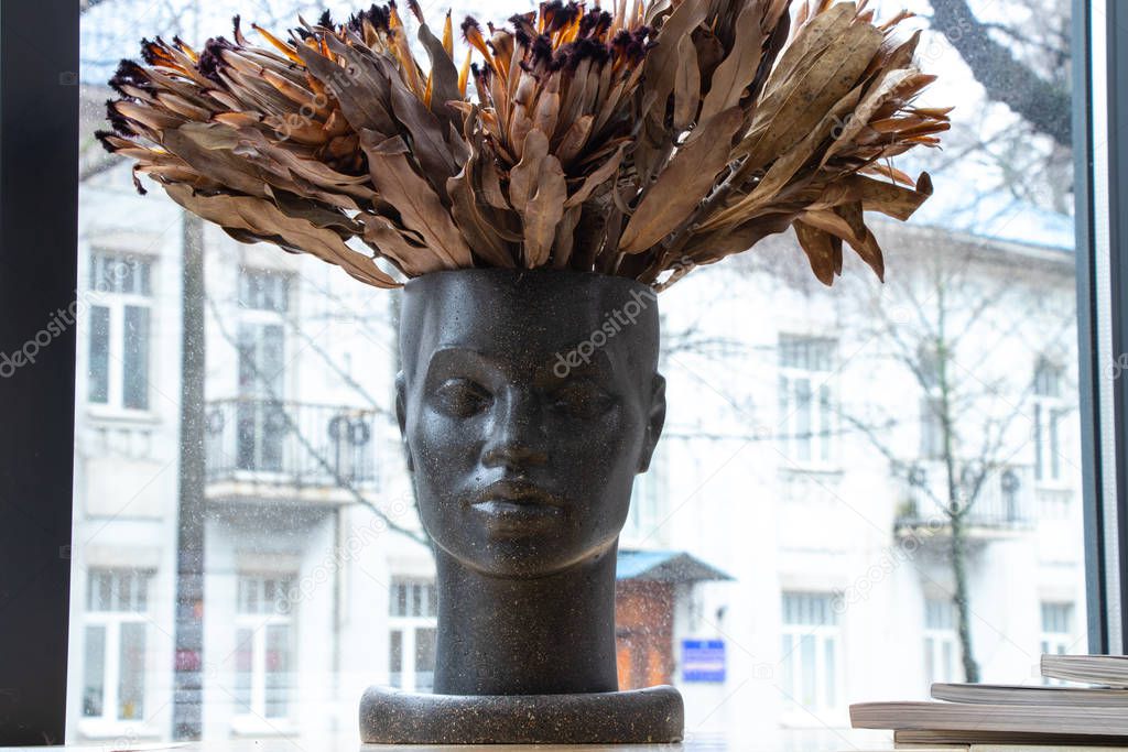 vase in the shape of a person's face with a bouquet of dried exotic flowers