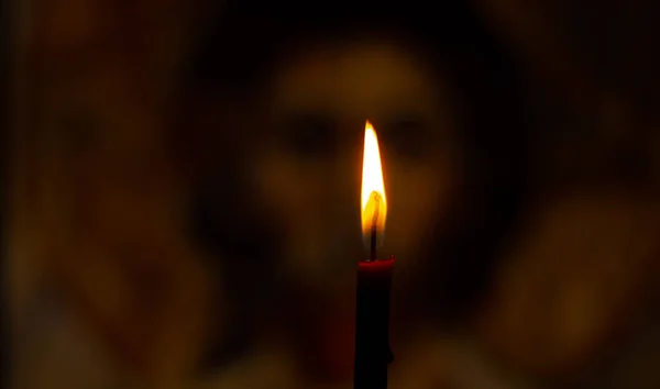 burning candle illuminates the icon of Jesus Christ in the dark
