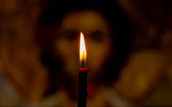 burning candle illuminates the icon of Jesus Christ in the dark