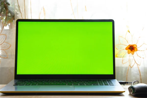 Un ordenador portátil con una pantalla verde está sobre la mesa en la habitación cerca de la ventana — Foto de Stock