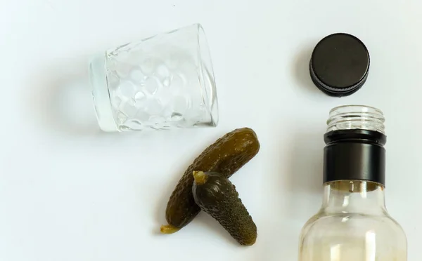 Vodka bottle next to a shot glass and two pickled cucumbers on a white background — Stock Photo, Image