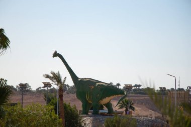 Mısır 'da güneş altında bir parkta büyük bir dinozor heykeli duruyor.