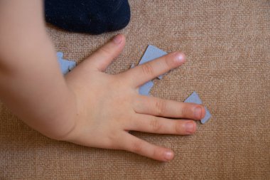 Çocuk eli, kahverengi fayans görünümlü zeminde bulmaca toplar.