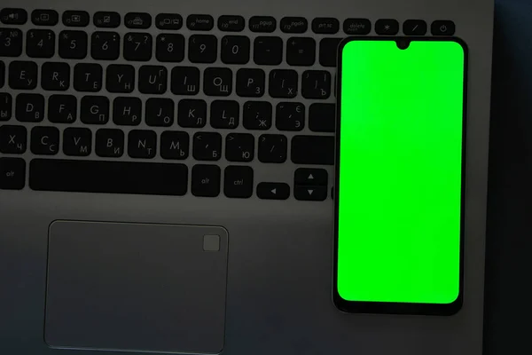 桌上放着一个绿色屏幕和一部触摸式电话的笔记本电脑 — 图库照片