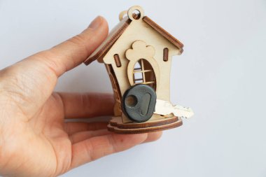 Tahta küçük oyuncak evi beyaz arka planda bir kadının elini tutuyor.