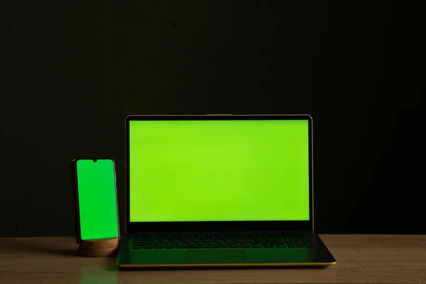a laptop with a green screen and a touch phone is on the table