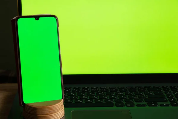 a laptop with a green screen and a touch phone is on the table