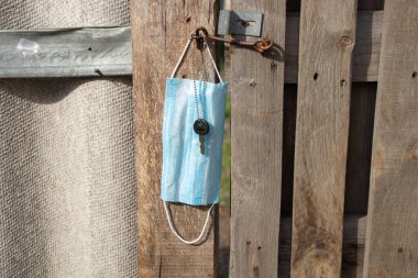 medical mask hanging on a hook and a door key on an old wooden gate in Ukraine on the street during clipart