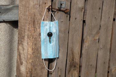 Tıbbi maske kancaya asılı ve kapı anahtarı Ukrayna 'da eski bir ahşap kapının üzerinde.