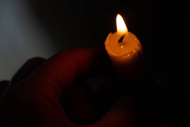 Karanlık bir odada yanan bir mum tutan el.