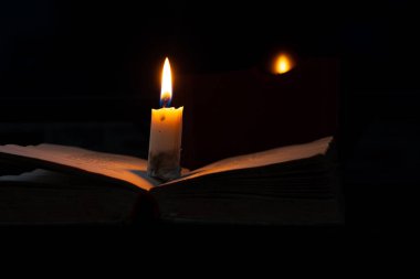 Karanlık bir odada yanan bir mum bir kitabın üzerinde duruyor.