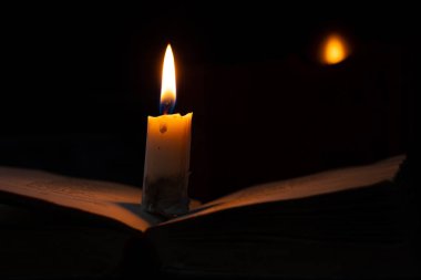 Karanlık bir odada yanan bir mum bir kitabın üzerinde duruyor.