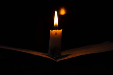 Karanlık bir odada yanan bir mum bir kitabın üzerinde duruyor.