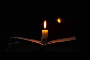 Karanlık bir odada yanan bir mum bir kitabın üzerinde duruyor.