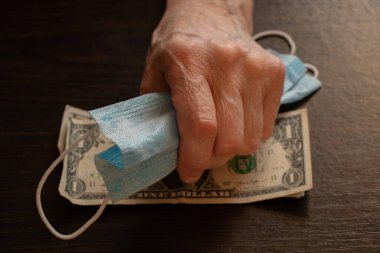 Tıbbi maske ve Amerikan doları yaşlı bir kadının ellerinde.