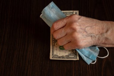 Tıbbi maske ve Amerikan doları yaşlı bir kadının ellerinde.