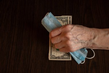 Tıbbi maske ve Amerikan doları yaşlı bir kadının ellerinde.