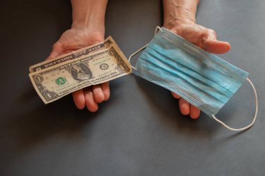 Tıbbi maske ve Amerikan doları yaşlı bir kadının ellerinde.