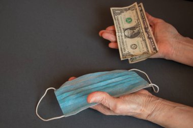 Tıbbi maske ve Amerikan doları yaşlı bir kadının ellerinde.