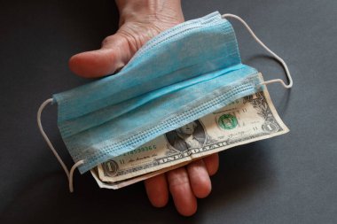 Tıbbi maske ve Amerikan doları yaşlı bir kadının ellerinde.