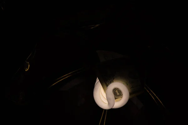 energy-saving light bulb with one American dollar in an old chandelier on the ceiling in a dark room