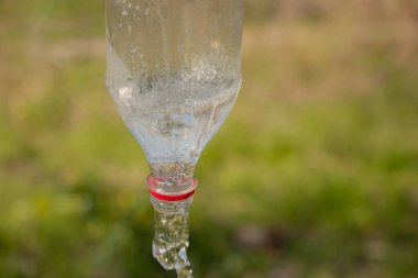 Su, sokakta bulanık yeşil arka planda plastik bir şişeden dökülüyor.