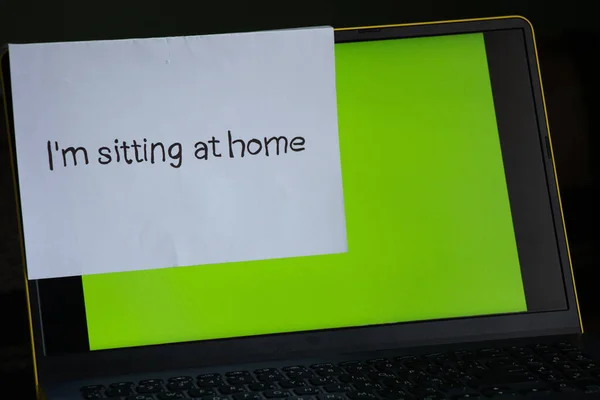 laptop with a green screen on a table in a room at home and a sheet with an inscription in English sitting at home in the period.
