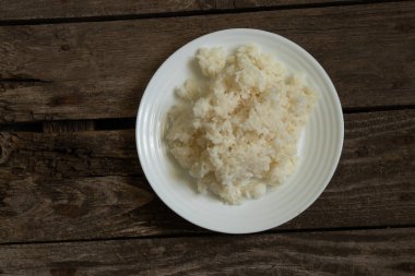 Eski ahşap bir tahtanın üzerinde haşlanmış pirinçli beyaz tabak.