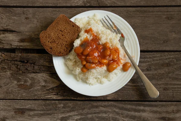 white plate with boiled rice and beans with bread on an old wooden board