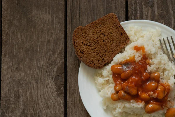 white plate with boiled rice and beans with bread on an old wooden board