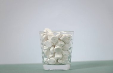 Masanın üzerinde beyaz yuvarlak tabletler olan cam bardak.
