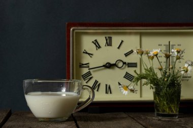 Bir fincan süt ve bir vazo, üzerinde papatyalar olan tahta bir masa.