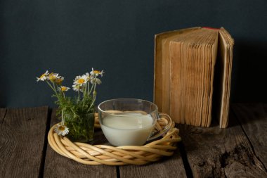 Bir bardak süt ve sabah kahvaltı için masanın üstünde papatyalar ve bir kitabın yanında...