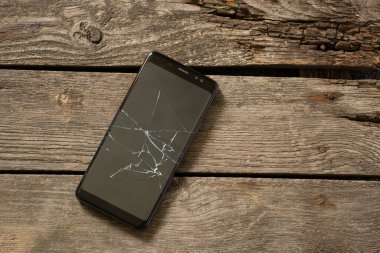 Ahşap arka planda çatlak ekranlı siyah telefon.