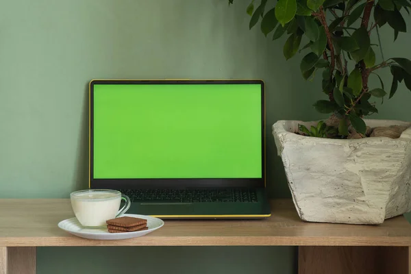 laptop with green screen yogurt with cookies on a table in a room at home