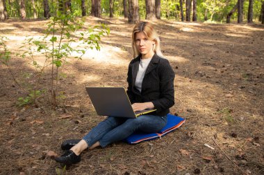 Ukraynalı kız, karantina altındaki kozalaklı bir ormanda dizüstü bilgisayarla oturuyor.