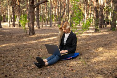 Ukraynalı kız, karantina altındaki kozalaklı bir ormanda dizüstü bilgisayarla oturuyor.