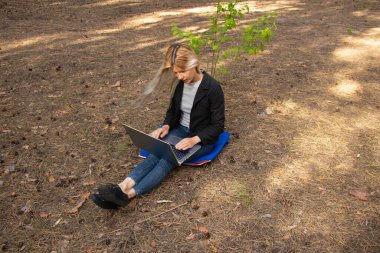 Ukraynalı kız, karantina altındaki kozalaklı bir ormanda dizüstü bilgisayarla oturuyor.