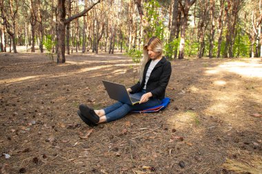 Ukraynalı kız, karantina altındaki kozalaklı bir ormanda dizüstü bilgisayarla oturuyor.