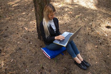 Ukraynalı kız, karantina altındaki kozalaklı bir ormanda dizüstü bilgisayarla oturuyor.