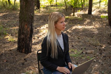 Ukraynalı kız, karantina altındaki kozalaklı bir ormanda dizüstü bilgisayarla oturuyor.