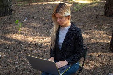 Ukraynalı kız, karantina altındaki kozalaklı bir ormanda dizüstü bilgisayarla oturuyor.