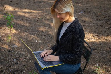 Ukraynalı kız, karantina altındaki kozalaklı bir ormanda dizüstü bilgisayarla oturuyor.