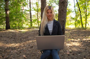 Ukraynalı kız, karantina altındaki kozalaklı bir ormanda dizüstü bilgisayarla oturuyor.
