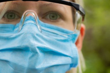 Tıbbi maskeli ve gözlüklü bir kız salgın sırasında sokakta yakın plan çekilmiş.