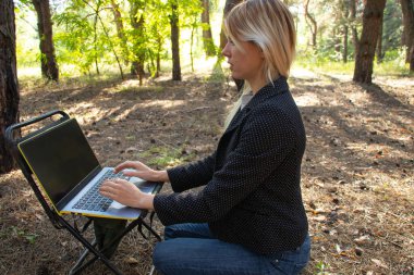 Ukraynalı kız, karantina altındaki kozalaklı bir ormanda dizüstü bilgisayarla oturuyor.