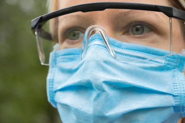 girl in a medical mask and glasses on the street close-up during a pandemic
