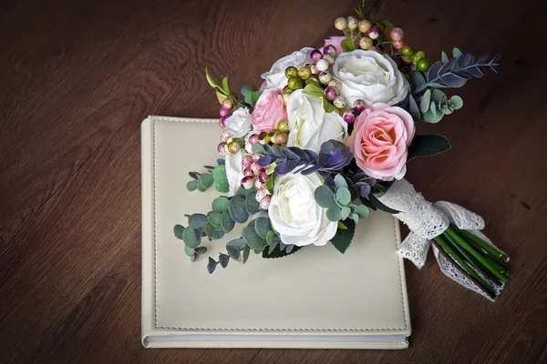A bouquet of artificial flowers lies on the wedding photo book 1 — Stock Photo, Image