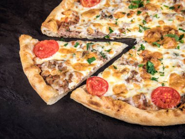 Etli, domatesli ve peynirli pizza. Bir dilim pizza pizzanın yanında duruyor.